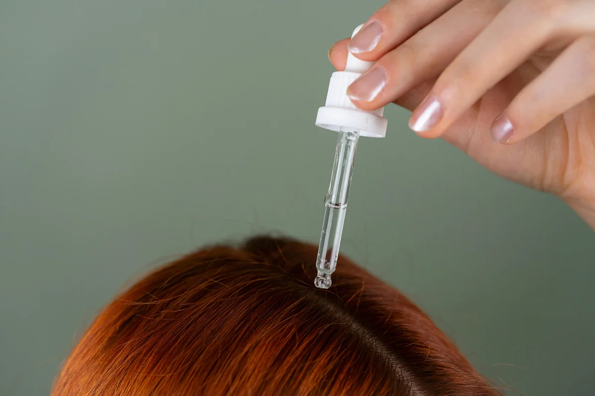 Person applying jojoba oil to their scalp in a bathroom mirror Person applying jojoba oil to their scalp in a bathroom mirror